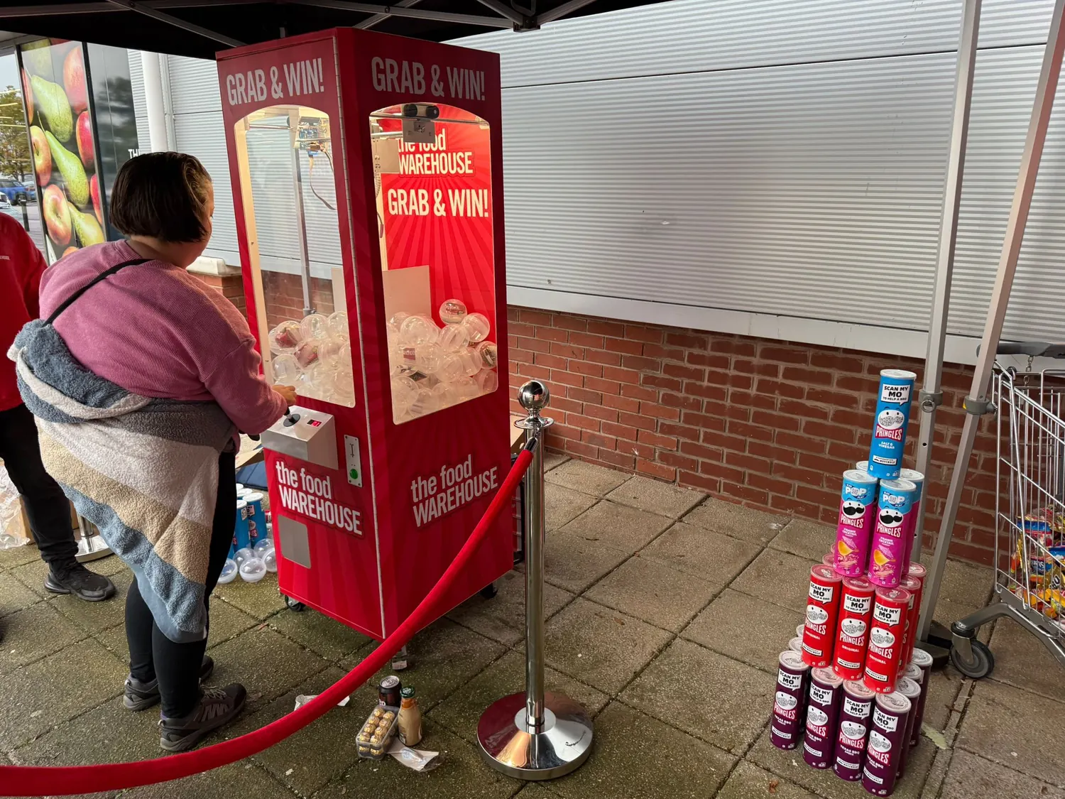 Visitor playing a grab and win claw machine at an outdoor promotion